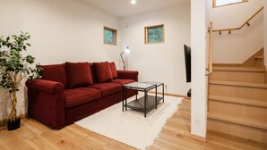 A living room with a red sofa, a glass coffee table, a white rug, a potted plant, and a staircase. - Villars Chalet (Hakuba)