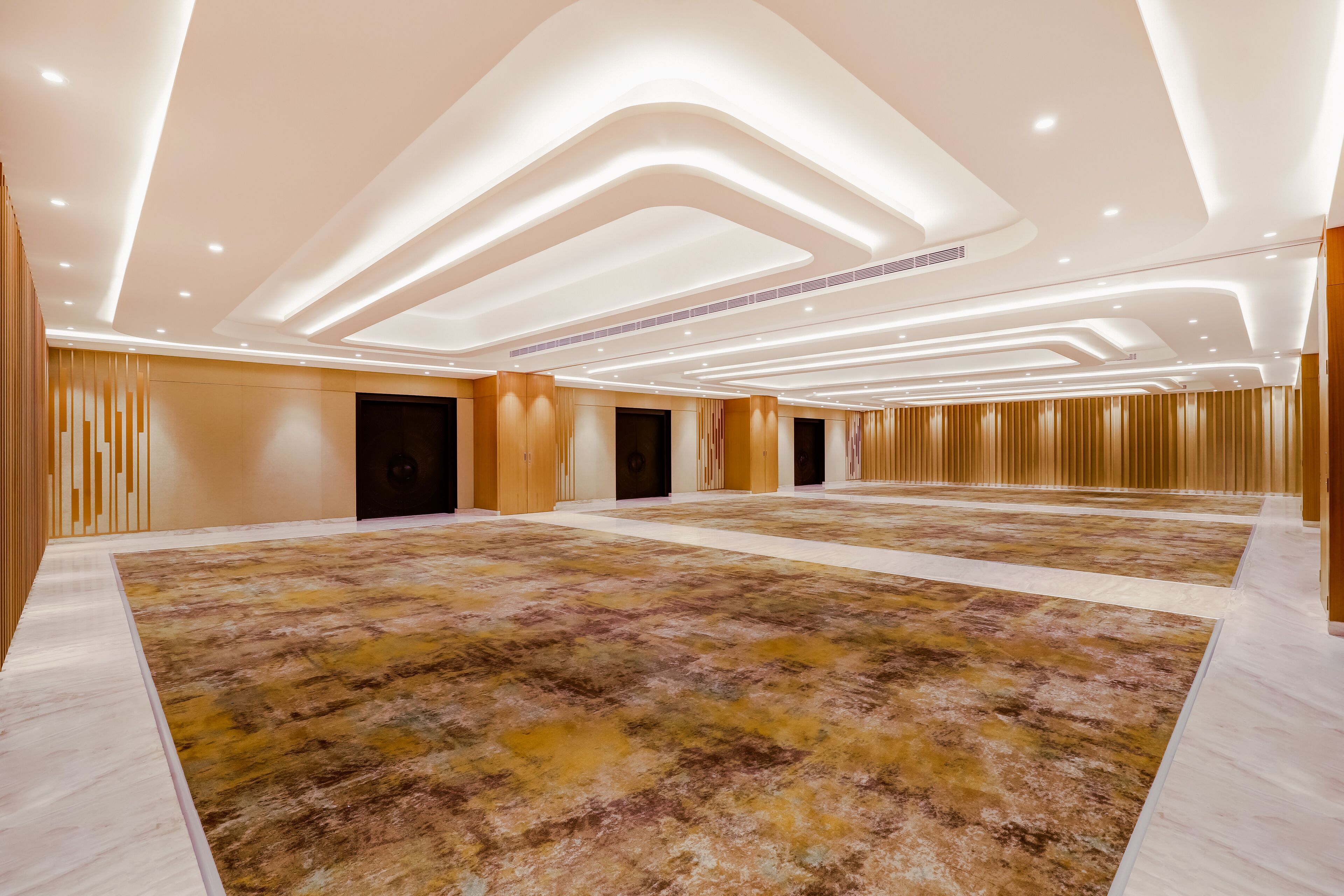 A spacious hotel lobby with a large carpeted area, multiple doors, and a modern ceiling design.