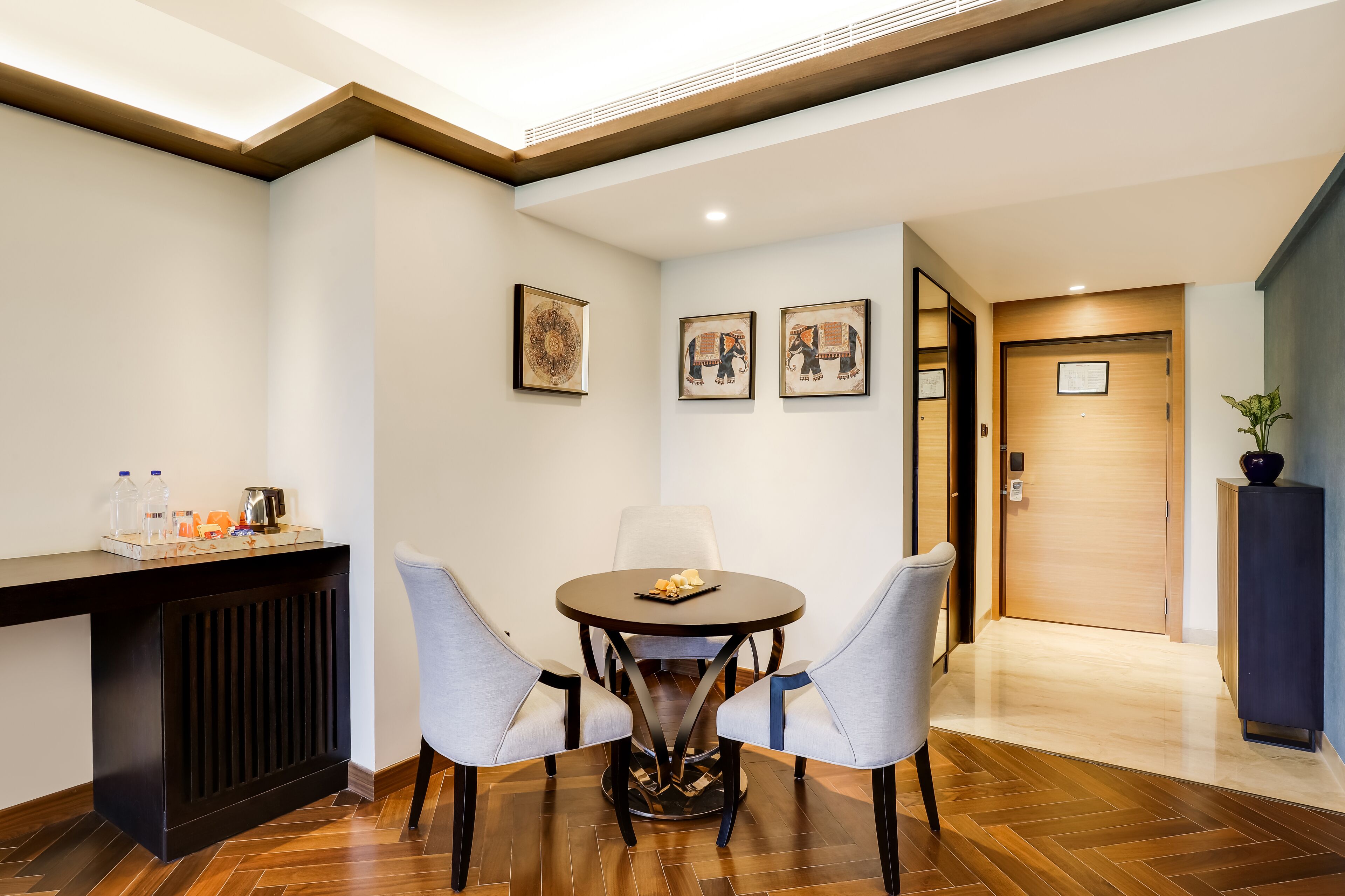 Un vestíbulo de hotel con una mesa de comedor redonda, dos sillas, una consola oscura con una bandeja y cuadros en la pared.