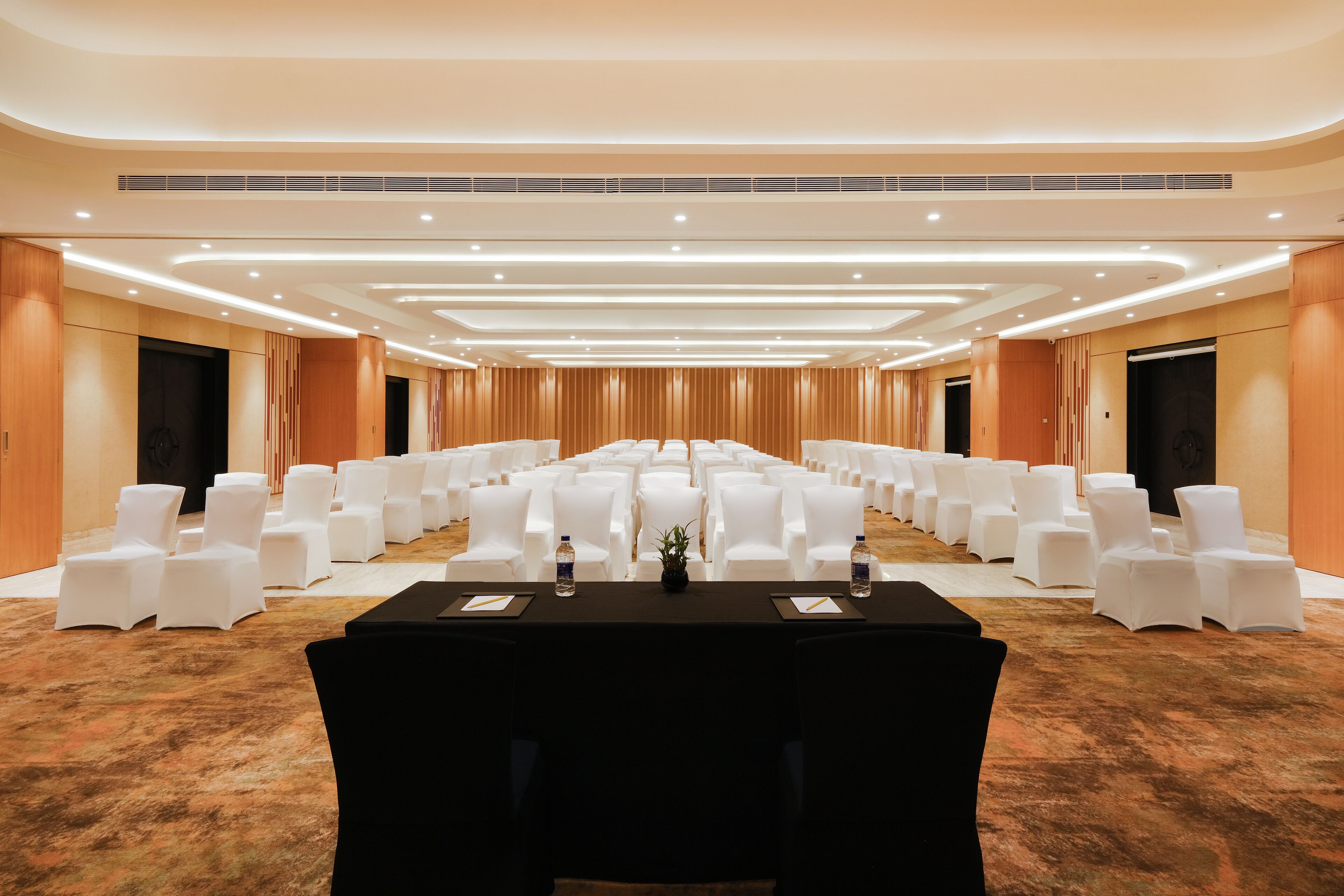 A conference room with rows of white chairs, a long table with black tablecloths, and a carpeted floor.