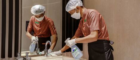 Two individuals cleaning a bathroom sink with a spray bottle and a tissue box.