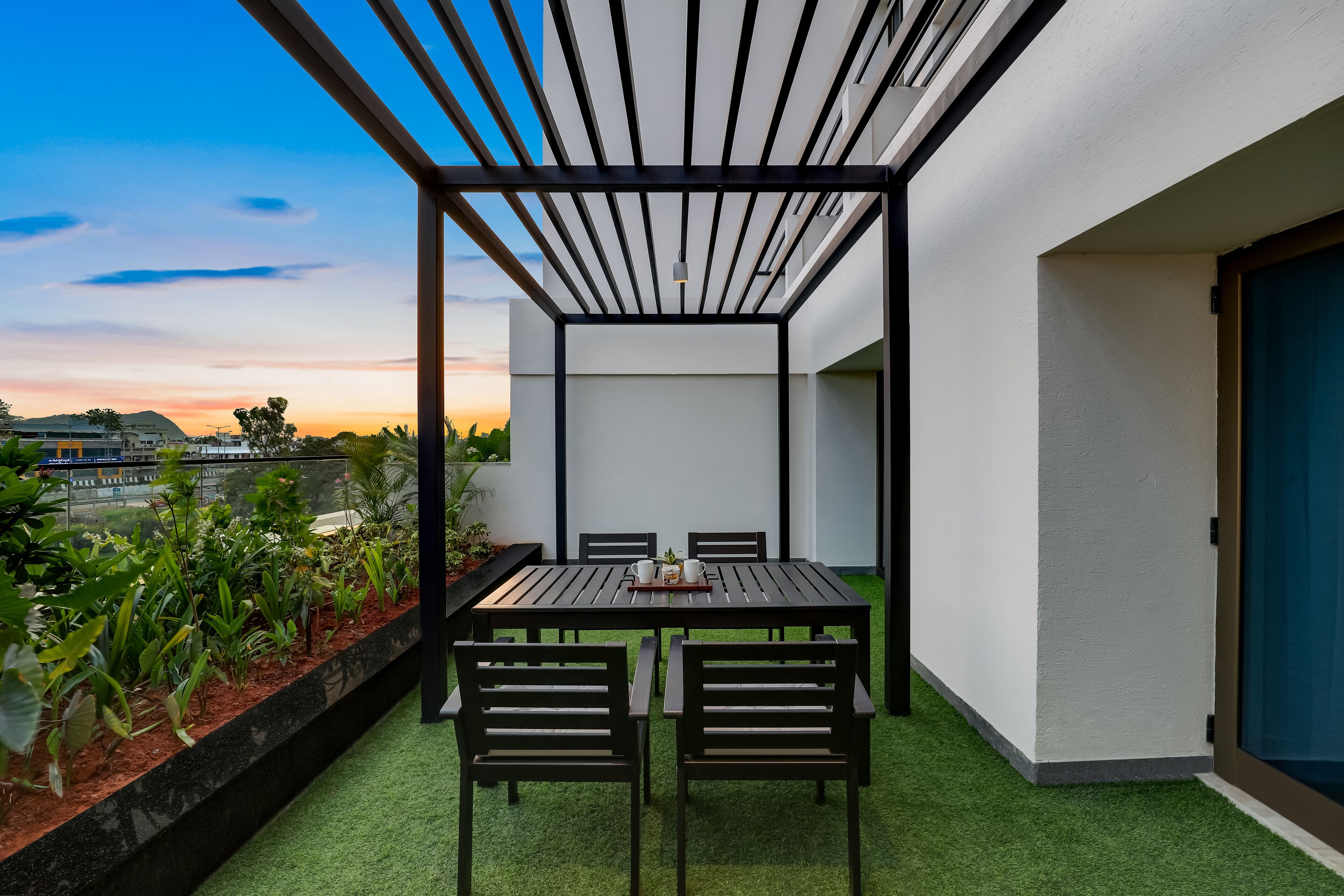 Een modern terras buiten, met een tafel en stoelen, omgeven door een witte muur en uitzicht op de zonsondergang.
