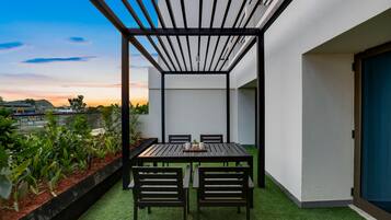Een modern terras buiten, met een tafel en stoelen, omgeven door een witte muur en uitzicht op de zonsondergang.