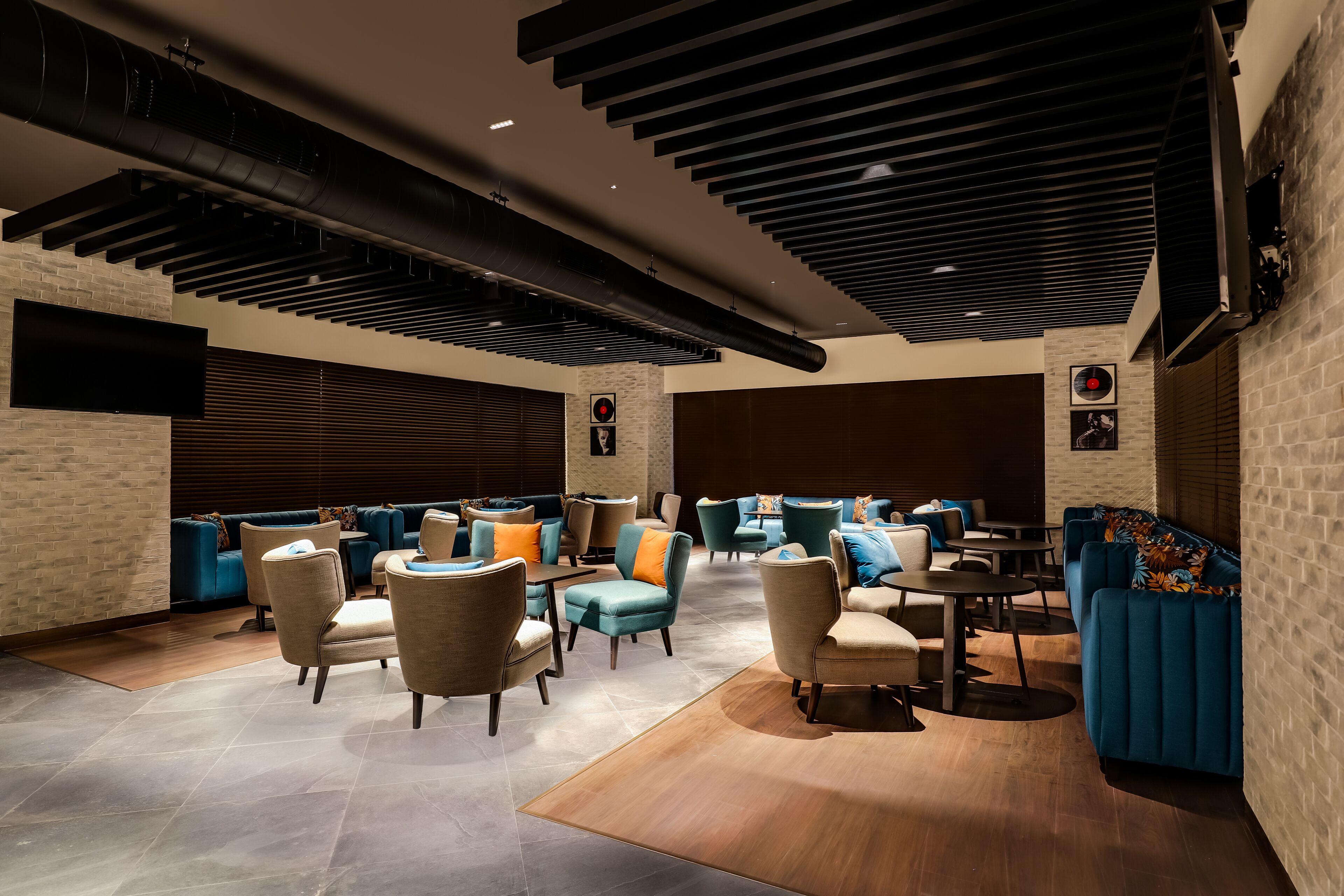 A modern lounge area with sofas, armchairs, and tables, featuring exposed ductwork and brick walls.