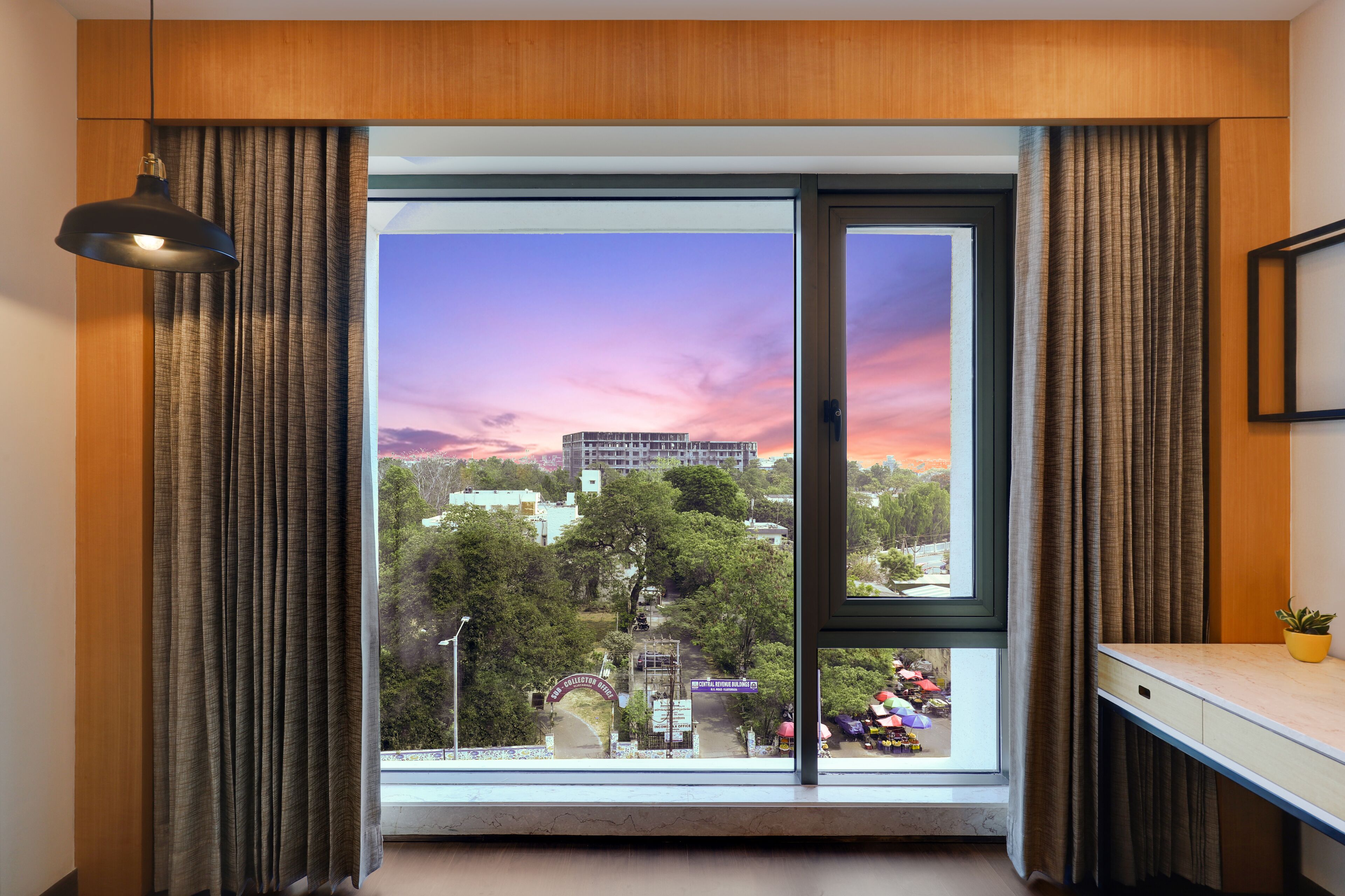 A room with a large window, curtains, a desk, and a hanging light fixture.