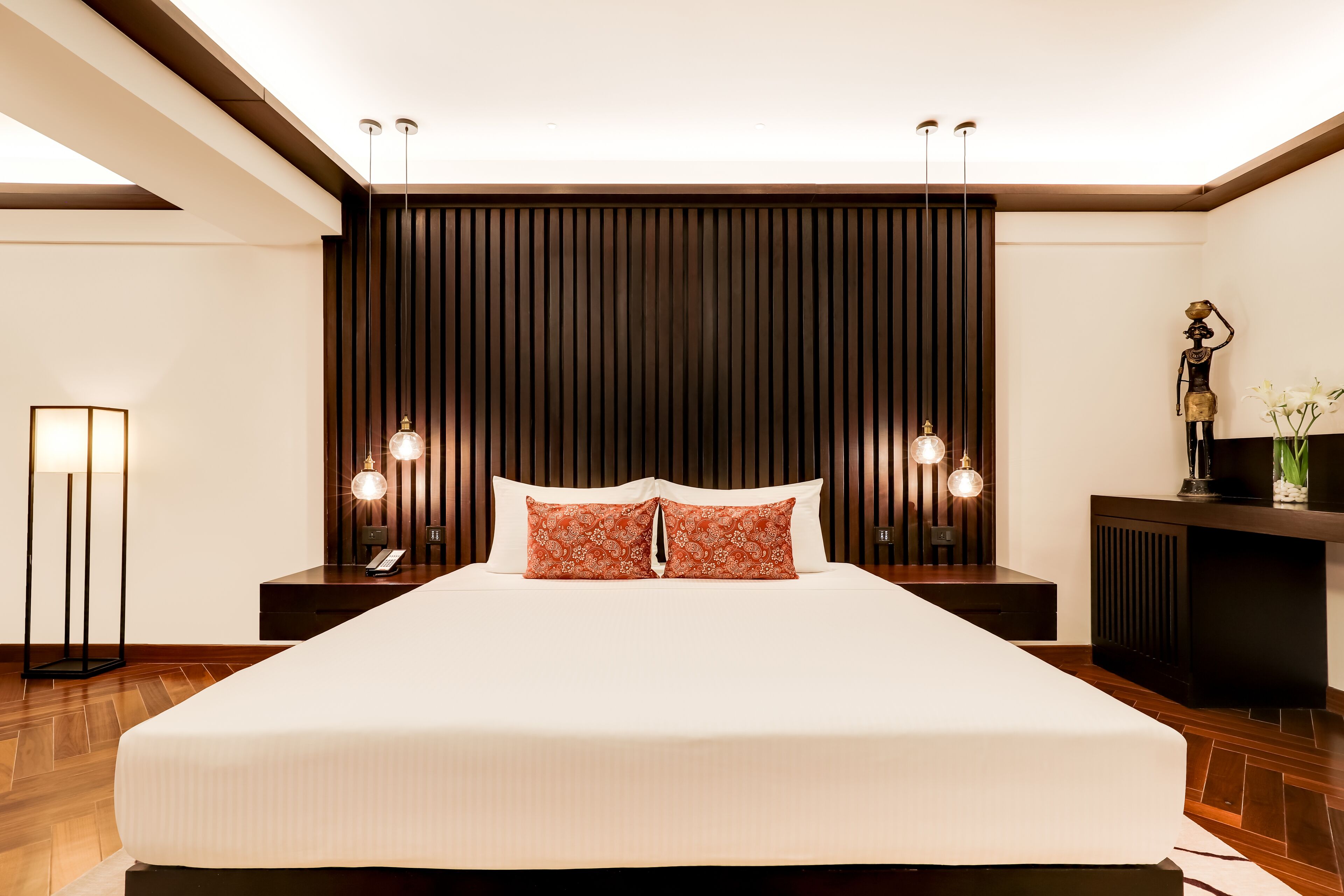 A neatly made bed with white linens and two decorative pillows, flanked by wooden headboards and nightstands with lamps.
