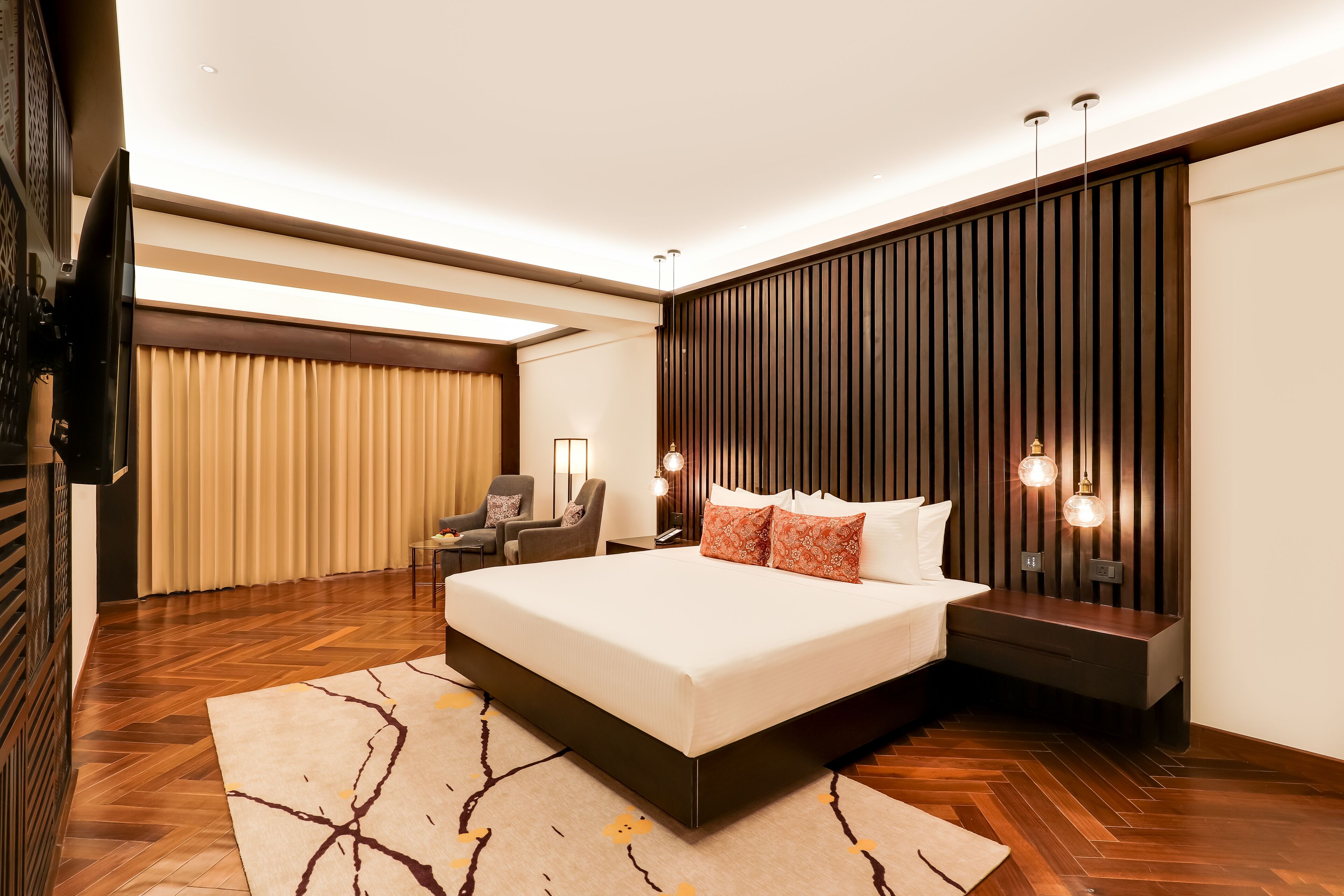 Ein modernes Hotelzimmer mit einem großen Bett, Holzböden, einem Fernseher, einem Schreibtisch und einer Wandleuchte.