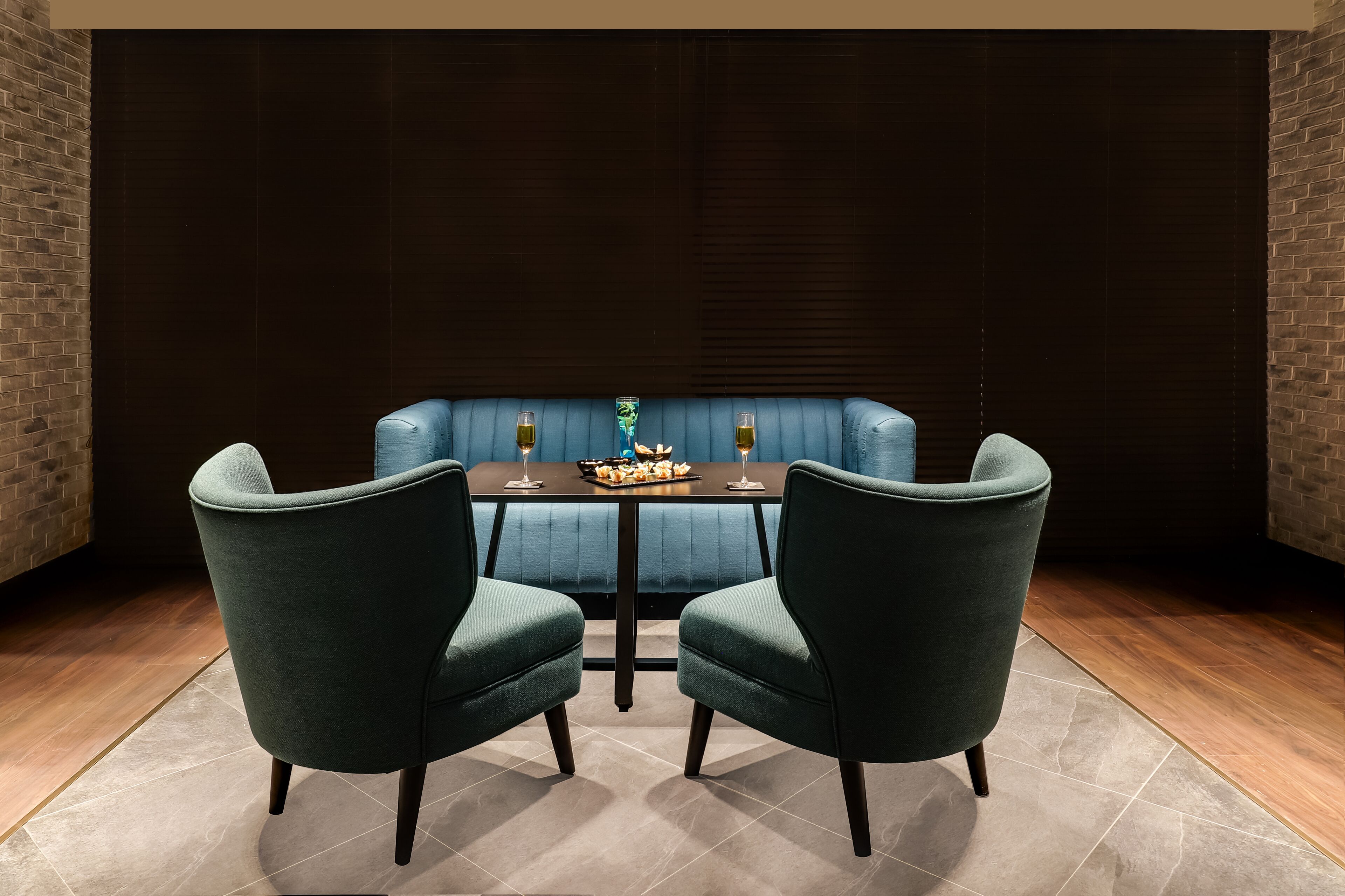 A dining area with a dark wooden wall, a blue cushioned bench, and two green upholstered chairs.
