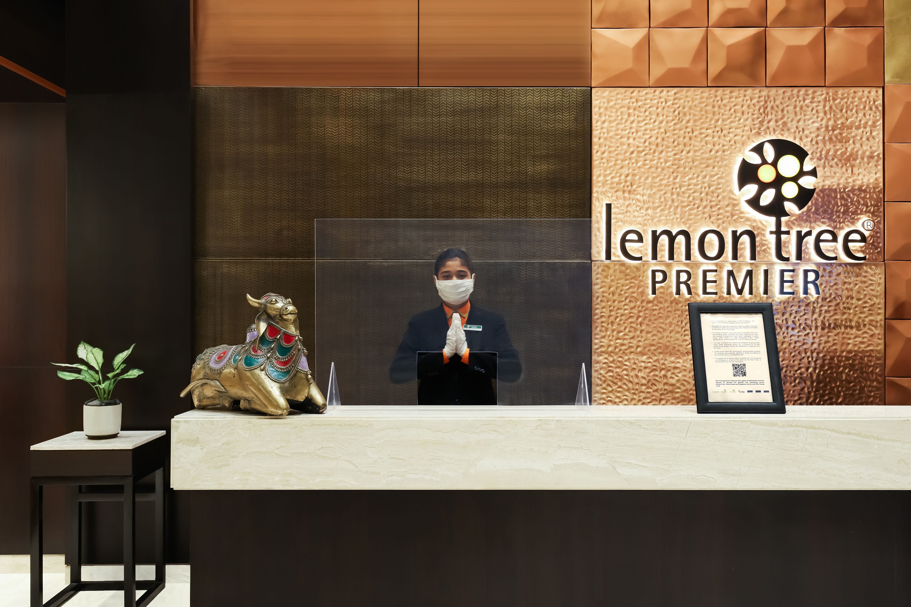 Taulell de recepció amb recepcionista, certificat emmarcat, planta en test i estàtua daurada decorativa.