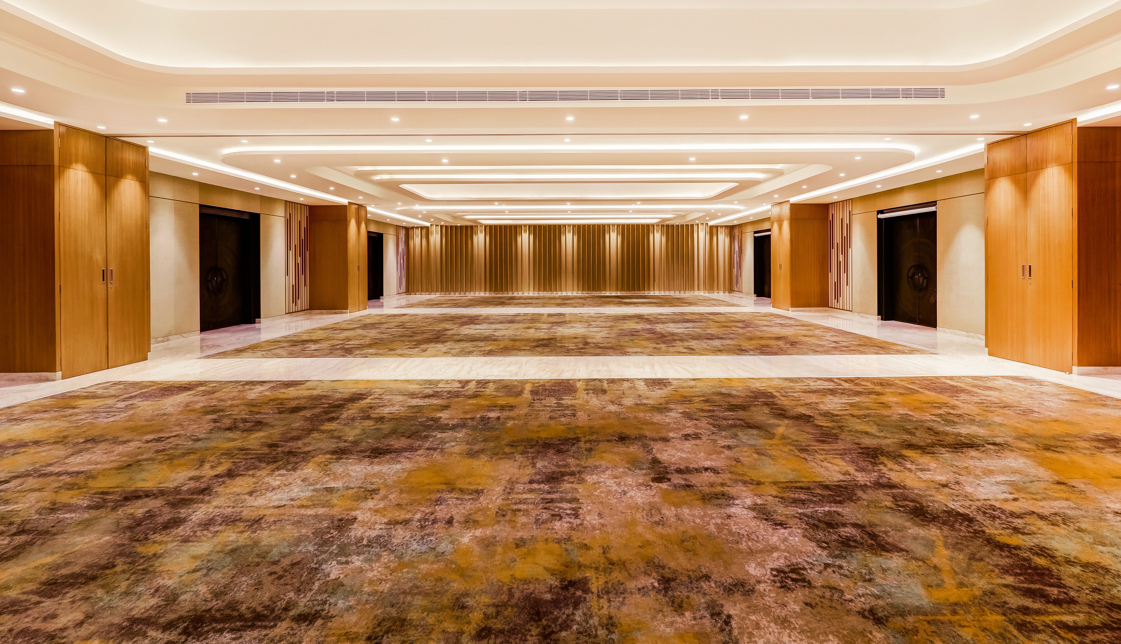 A spacious hallway with a patterned carpet, wooden panel walls, and recessed lighting.