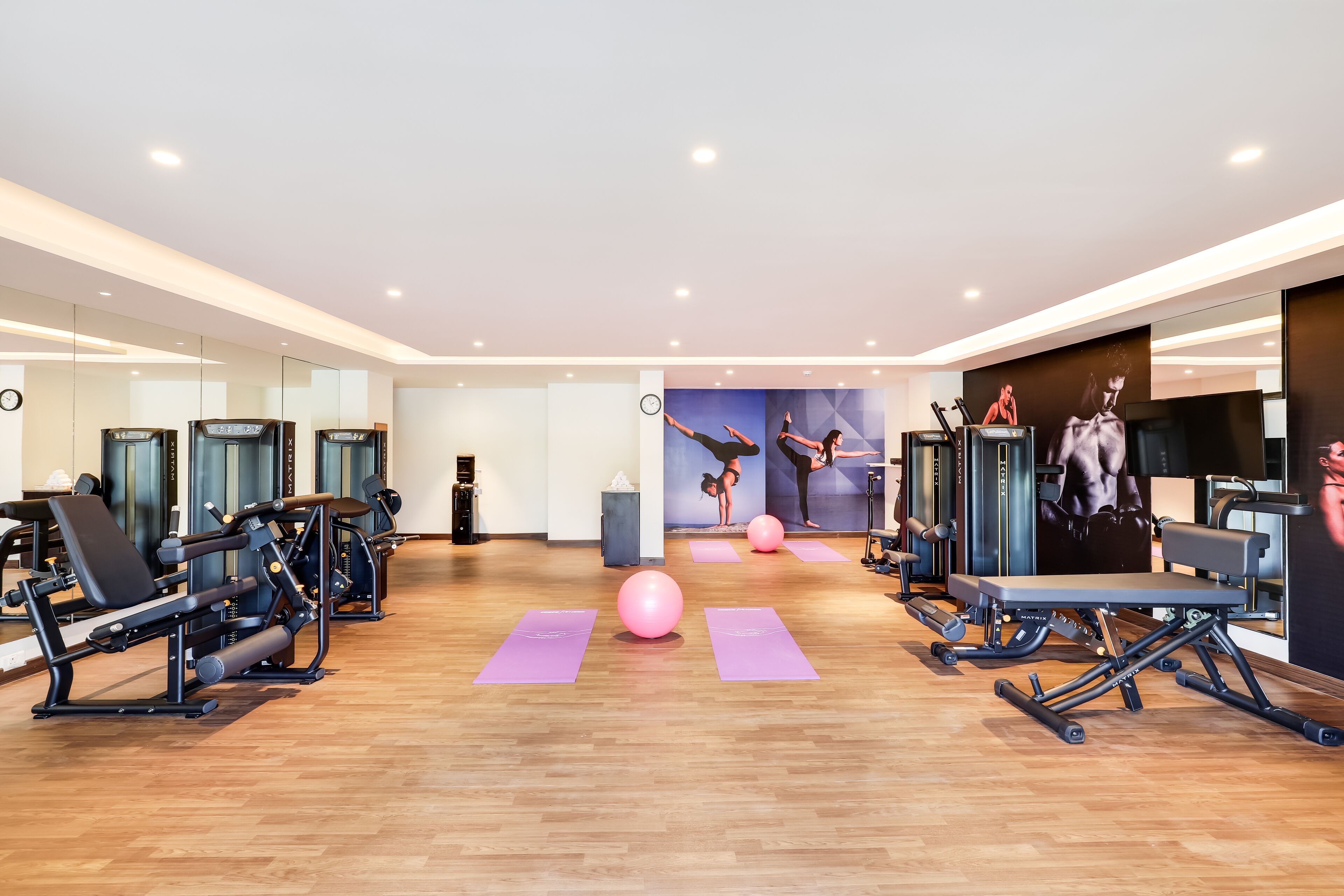 Een moderne sportschool met diverse fitnessapparaten, waaronder krachttrainingsmachines en cardioapparaten, gerangschikt op een houten vloer met paarse matten.