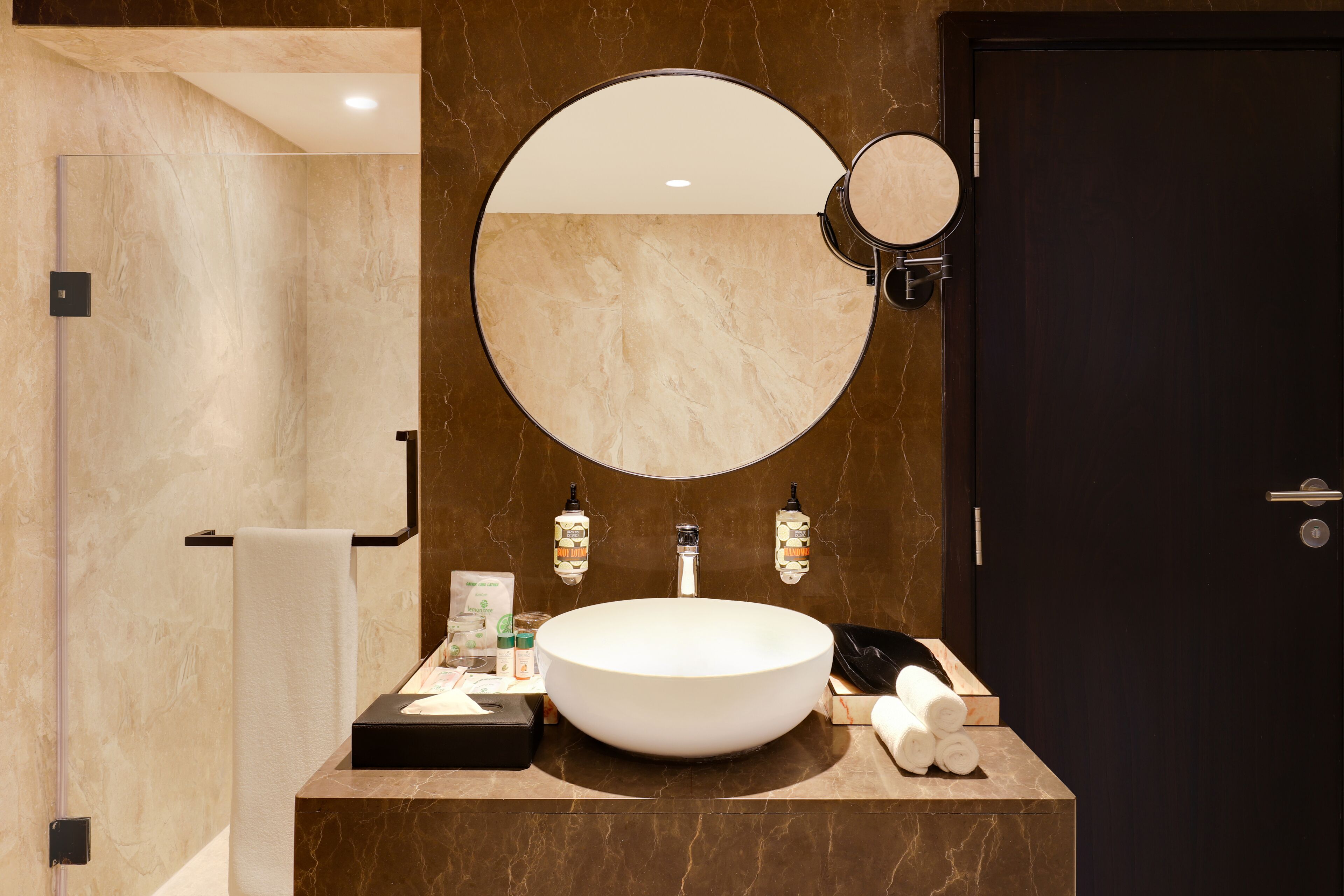 Un baño moderno con un espejo redondo grande, un lavabo blanco y una puerta oscura.