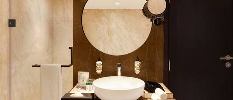Un baño moderno con un espejo redondo grande, un lavabo blanco y una puerta oscura.