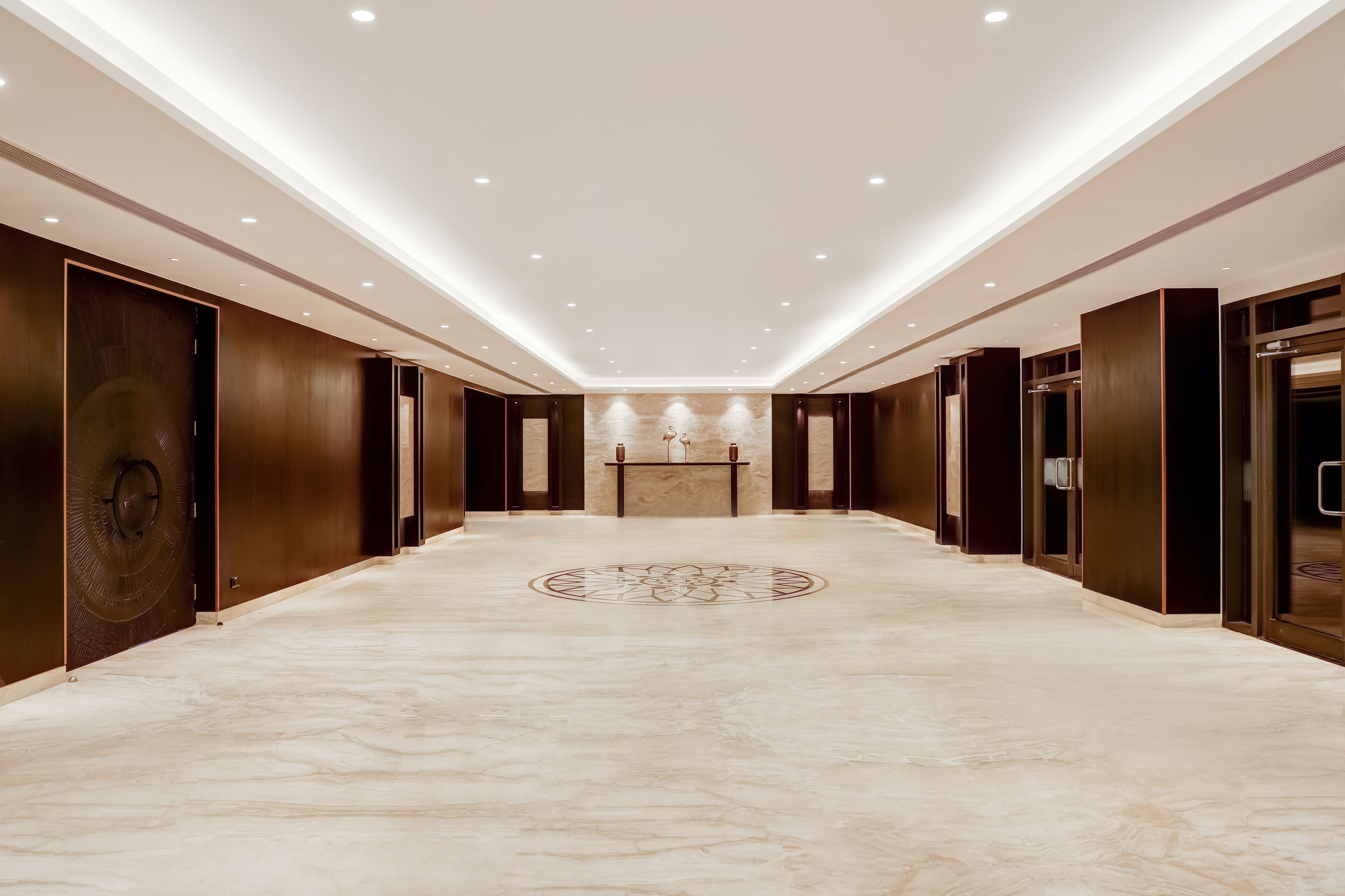 A spacious, well-lit hallway with a marble floor and wooden paneling, leading to a reception area with a decorative emblem.