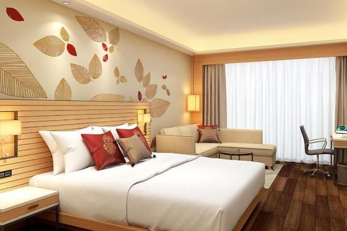 A hotel room with a large bed, a desk, a chair, and a sofa.
