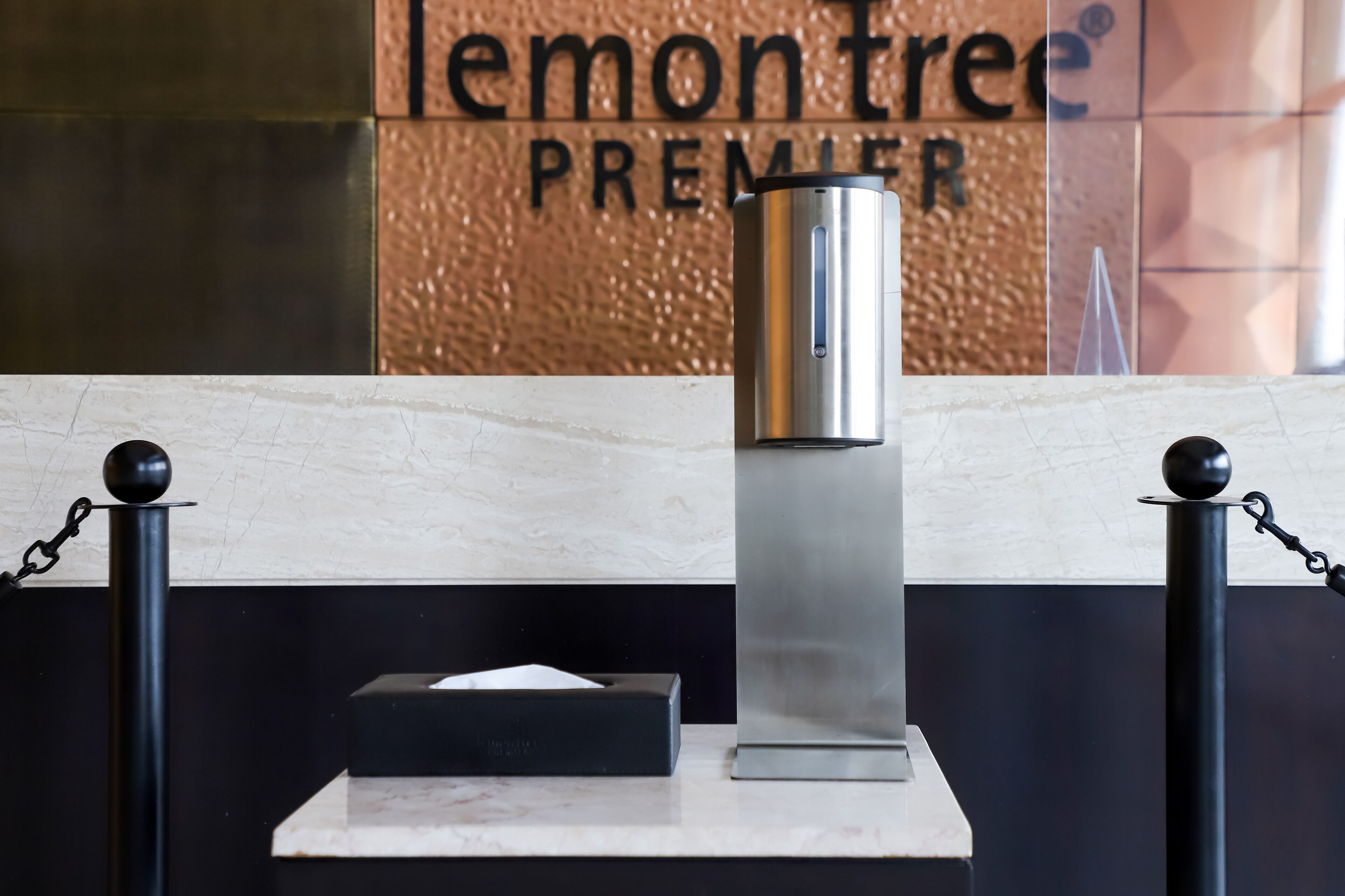 A modern hotel reception area with a metallic object on a pedestal, a black tissue box, and a sign reading "lemon tree PREMIER".