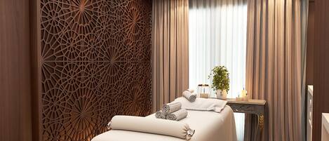 Un hotel moderno con una cama grande, una pared decorativa, una pequeña mesa con velas y vistas al exterior.