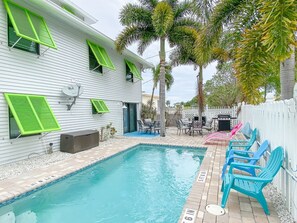 A swimming pool with a tiled deck, surrounded by a white fence and palm trees.