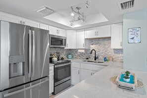 A modern kitchen with stainless steel appliances, white cabinetry, a tiled backsplash, and a small potted plant on the counter. - 🐾 Pet Friendly, Heated Pool, Gorgeous Renovation, Walk to the sugar sand of FMB! (Fort Myers Beach)