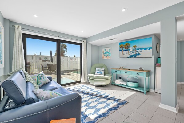 A modern living room with a sofa, a teal console table, and a large window overlooking a deck.