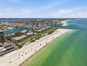 An aerial view of a coastal city with a long sandy beach, adjacent high-rise buildings, and a marina.