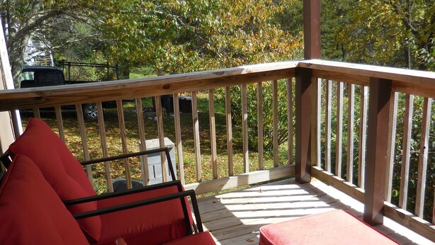 A wooden deck with red chairs and a table, overlooking a wooded area. - BACK TO THE 50'S GUEST HOUSE (Princeton, WV 24739)