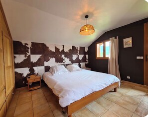 Una camera da letto con un letto grande, un comodino, un'armadio in legno, una parete rivestita in pelle di vacca, una finestra con tende e un lampadario.