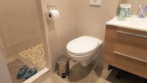 A bathroom with a toilet, a trash can, a toilet paper holder, and a sink with a toothbrush holder.
