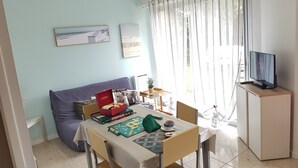 A living room with a sofa, a table with board games, a coffee table, a TV, and a window with curtains.