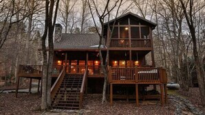 A cabin with a staircase leading to a balcony, surrounded by trees.