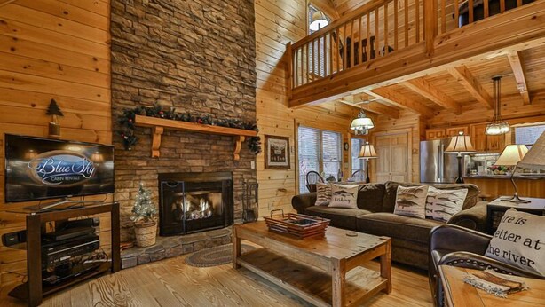 A cabin interior with a stone fireplace, wooden furniture, a television, and a balcony.