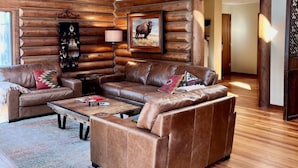 A log cabin interior with a large leather sofa, wooden flooring, a ceiling fan, and a framed animal picture. - Home in the Bitterroots (Victor)