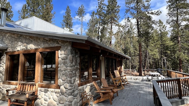 A rustic cabin with a stone exterior, wooden deck, and Adirondack chairs. - Home in the Bitterroots (Victor)
