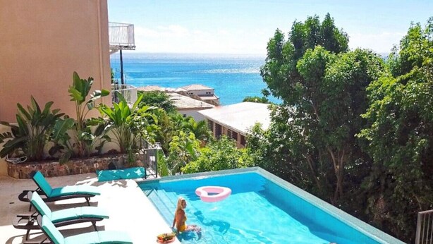 A swimming pool with lounge chairs, a view of the ocean, and lush greenery. - Seagrape 2 - 1 bedroom suite at Seagrape Vista (Cruz Bay)