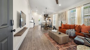 A spacious living area with a ceiling fan, a flat-screen TV, a wooden coffee table, and a sofa with orange cushions. - Casa del rancho in the EE - 3 km from FIFA Fest (Houston)