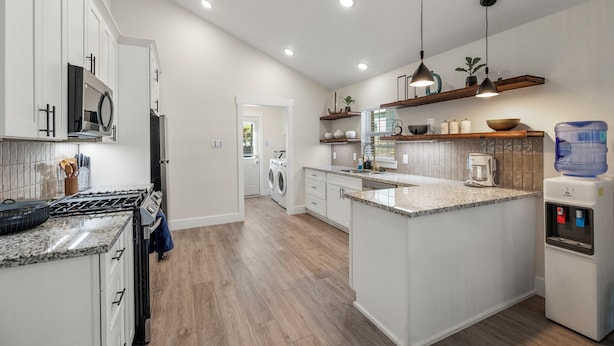A modern kitchen with white cabinets, granite countertops, a built-in stove, and a water dispenser. - Casa del rancho in the EE - 3 km from FIFA Fest (Houston)