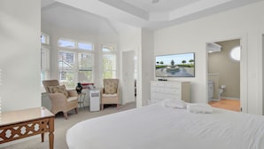 Un dormitorio con una cama grande, un televisor montado en la pared, un escritorio con silla y una ventana con persianas.