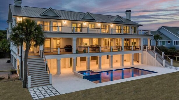 A large, two-story house with a swimming pool, multiple balconies, and a well-lit exterior at dusk. - Discounts!! Serenity- 2 50th One of a kind Oceanfront Master Piece, Pool/Hot Tub (Isle Of Palms)
