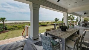 A covered outdoor area with a wooden table and chairs, a ceiling fan, and a view of the beach. - Discounts!! Serenity- 2 50th One of a kind Oceanfront Master Piece, Pool/Hot Tub (Isle Of Palms)