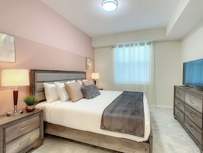 Un dormitorio con cama, mesitas de noche, televisión y ventana con cortinas.