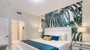 A bedroom with a large bed, white headboard, and a tropical leaf-patterned wall. - Modern Condo 5mi to Disney, Foosball, Giant Water Slide, Free Water Park (Kissimmee)