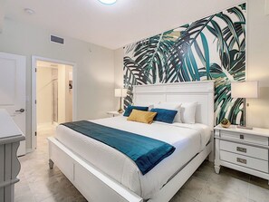 A bedroom with a large bed, white headboard, and a wall mural.