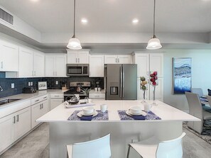 A modern kitchen with white cabinetry, stainless steel appliances, and pendant lighting.