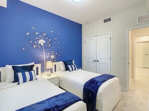 Ein Hotelzimmer mit zwei Betten, einem Nachttisch mit Lampe, einem Wandbild von Löwenzähnen und einer Tür rechts.