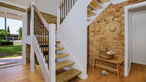 Een trap met houten treden en witte leuningen, die leidt naar een kamer met een bakstenen muur en een mandje op een klein tafeltje.