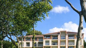 Um hotel com vários andares, varandas, um lago com nenúfares e vegetação ao redor.
