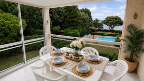 A dining area with a table set for four, surrounded by white chairs, on a balcony with a view of a swimming pool and greenery. - Exceptional sea view - Terrace & Pool (Pornic)