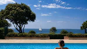 Uma piscina com vista clara para o mar e um veleiro ao longe.