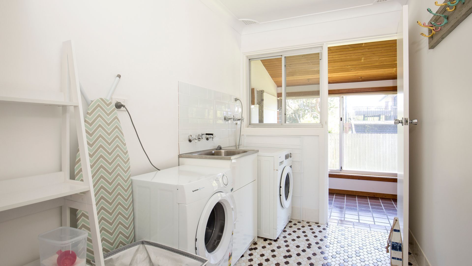 A compact laundry room with a washing machine, dryer, and a sink. There is a window with a view of the outside.