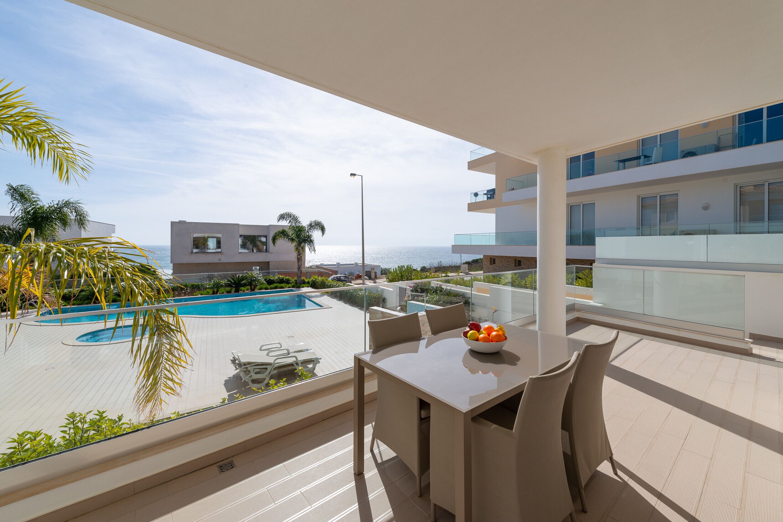 Un balcon avec une piscine, une table avec des chaises et une vue sur la mer.